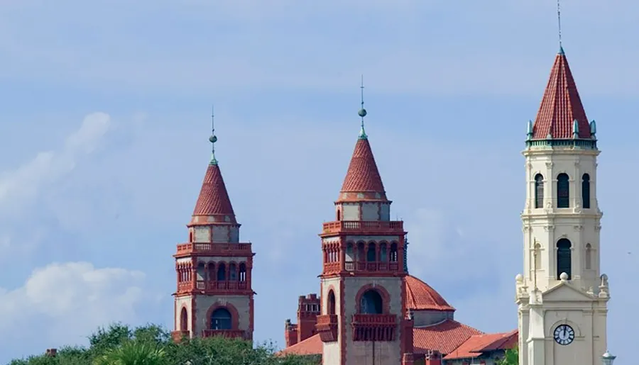 The image features three architectural towers with red roofs and intricate detailing against a backdrop of blue sky.