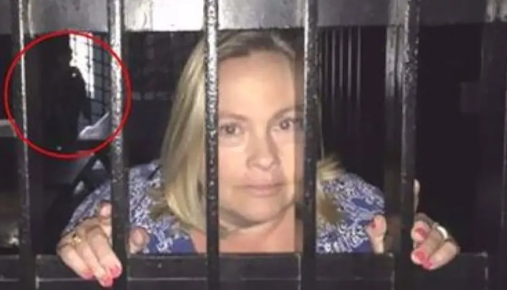 A woman is standing behind metal bars with a shadowy figure circled in the background