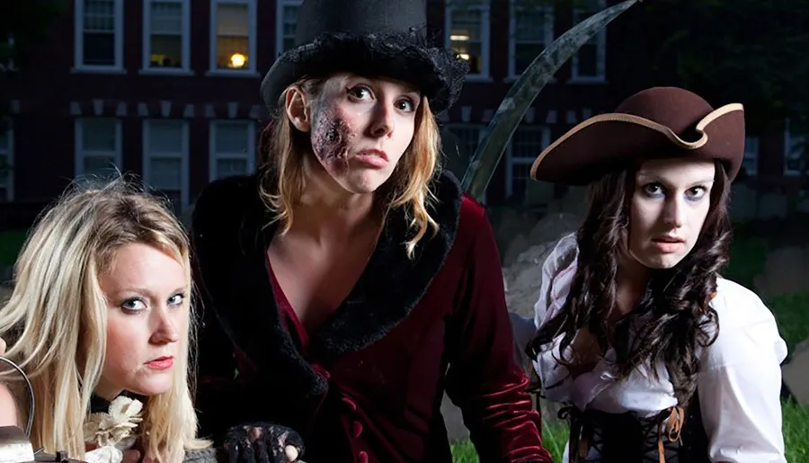 Three people dressed in elaborate pirate-themed costumes pose dramatically in front of a dark, ominous building.