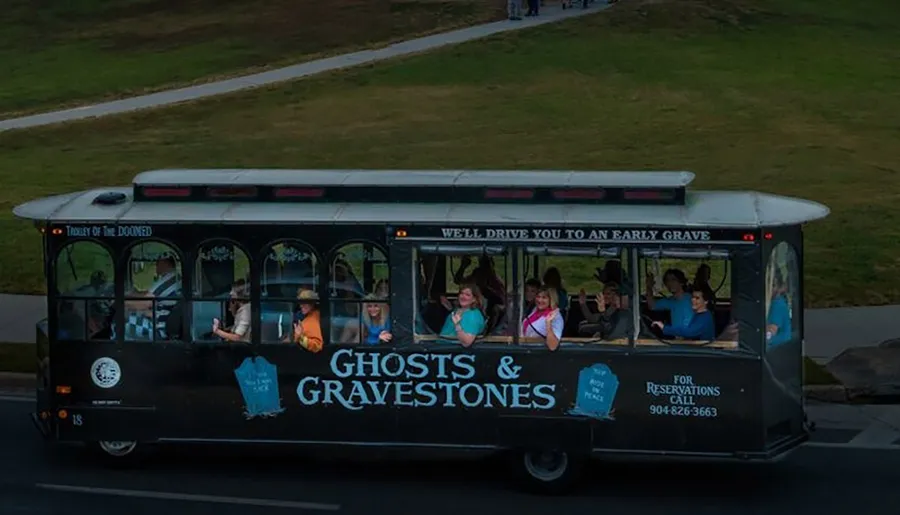 A trolley labeled Ghosts & Gravestones with passengers aboard is traveling along a grassy area.