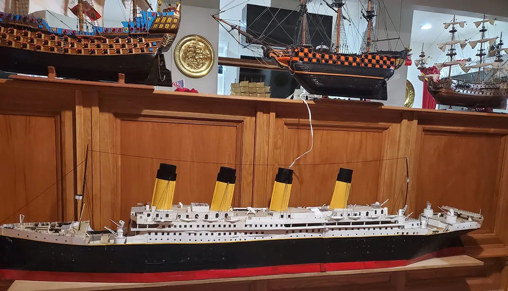 The image shows several intricately crafted ship models including a large ocean liner with yellow funnels displayed on wooden shelves