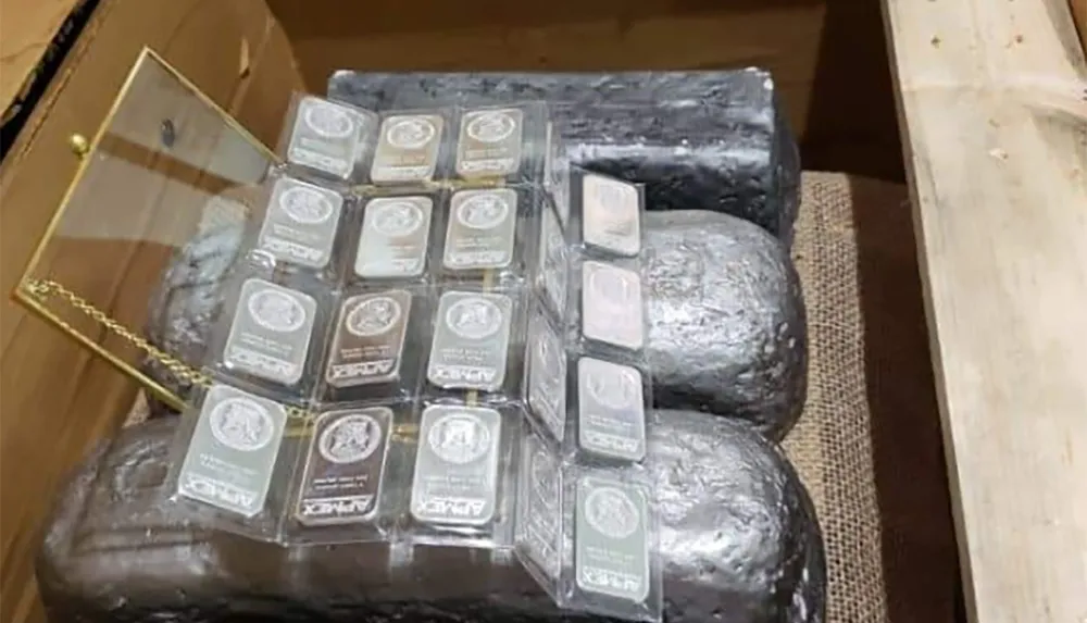 The image shows a collection of silver bars and a display of smaller precious metal bars placed on top of larger metal blocks inside a wooden crate