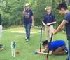Four people of varying ages are participating in a game of croquet on a green lawn