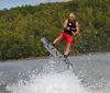 A person is captured mid-air while wakeboarding on a lake with a backdrop of trees