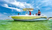 A group of people are enjoying a sunny day on a white and yellow Pro-Line motorboat near the shore with clear blue skies above them.