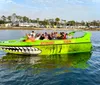 A group of people is enjoying a ride on a vibrant green speedboat with shark teeth graphics painted on the bow