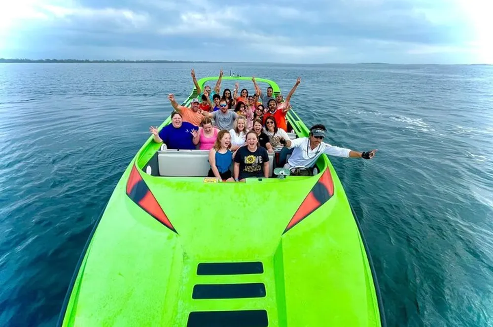 A group of cheerful people are posing with raised hands on a bright green speedboat on the water