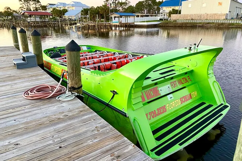 A bright green airboat is docked on a wooden pier with life jackets visible on the seats and residential buildings in the background