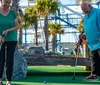 A family of four is enjoying a game of mini-golf on a sunny day with a ferris wheel and other attractions in the background