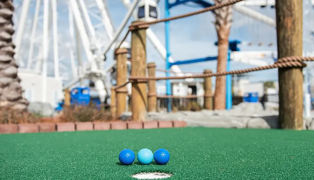 Three blue golf balls are placed on a miniature golf course with a blurred Ferris wheel in the background