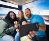 Three people are taking a smiling selfie inside a Ferris wheel cabin with a drinks and scenic coastal views in the background