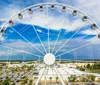 Three people are taking a smiling selfie inside a Ferris wheel cabin with a drinks and scenic coastal views in the background