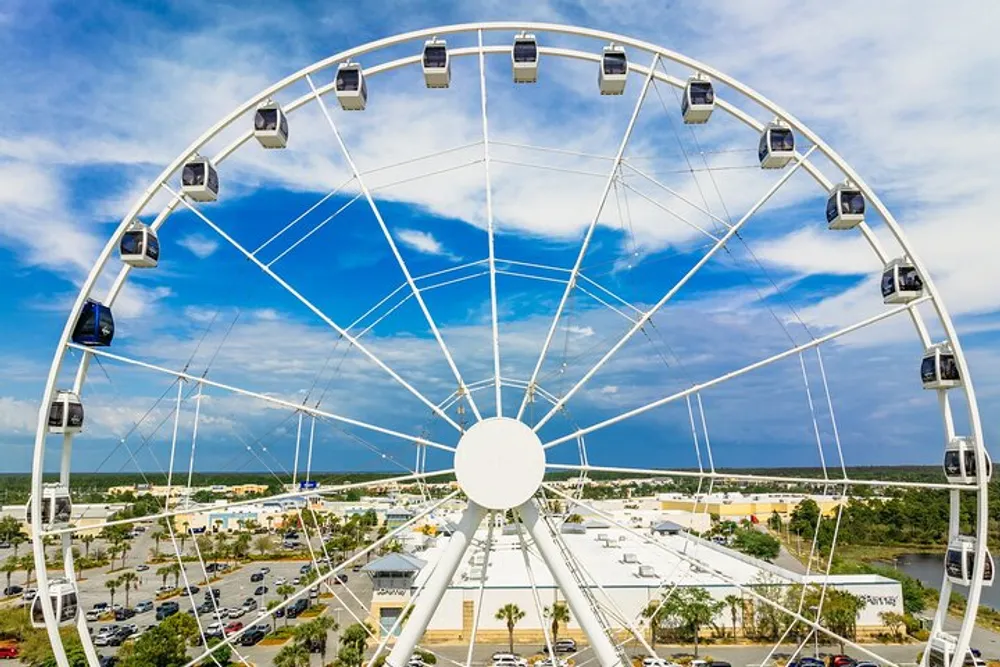 A large observation wheel with enclosed capsules stands against a partially cloudy sky offering a panoramic view of the surrounding area