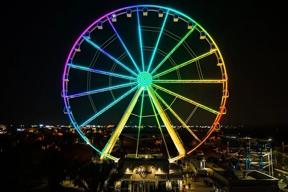 A brightly lit Ferris wheel illuminates the night with vibrant colors against a backdrop of a dark sky and city lights