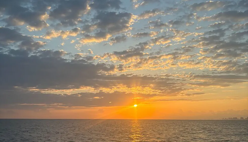 A serene sunset view over the ocean with scattered clouds reflecting the warm sunlight