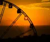 A silhouette of a Ferris wheel stands against a vibrant sunset over the ocean