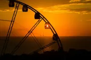 A silhouette of a Ferris wheel stands against a vibrant sunset over the ocean.