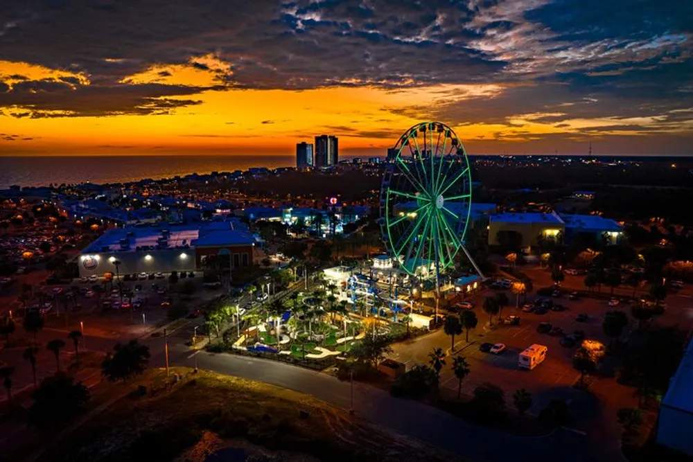 An illuminated Ferris wheel stands out against a dramatic sunset sky in a bustling urban area