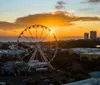 A silhouette of a Ferris wheel stands against a vibrant sunset over the ocean