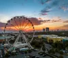 A silhouette of a Ferris wheel stands against a vibrant sunset over the ocean