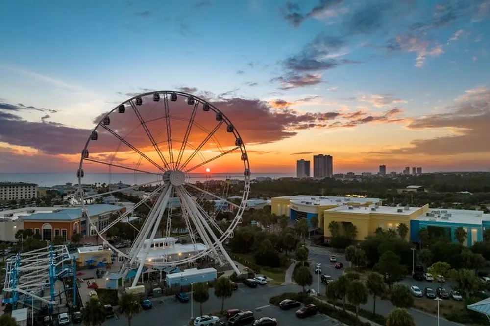 A Ferris wheel dominates the foreground against a beautiful sunset sky with silhouetted city buildings in the distance