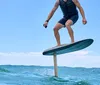 A persons feet are on a surfboard cutting through the water with mountains and a blue sky with clouds in the background