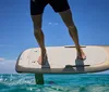 A persons feet are on a surfboard cutting through the water with mountains and a blue sky with clouds in the background