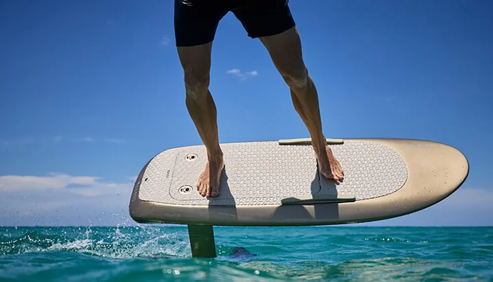 A person is hydrofoiling on a sunny day above the crystal-clear waters of the ocean