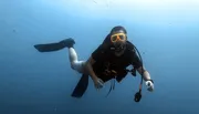 A diver with a prosthetic leg is swimming underwater equipped with fins, a diving mask, and a snorkel.