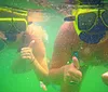 Two people are giving a thumbs-up while snorkeling underwater wearing masks and snorkels