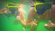 Two people are giving a thumbs-up while snorkeling underwater, wearing masks and snorkels.