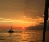 A sailboat with a black sail bearing a pelican image is cruising on the water at sunset with a group of passengers enjoying the scenery