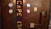 The image displays an industrial-themed room with brick walls, featuring a variety of analog gauges, a quarantine warning sign, and a pillar with text cutouts that cast shadows on the wall.