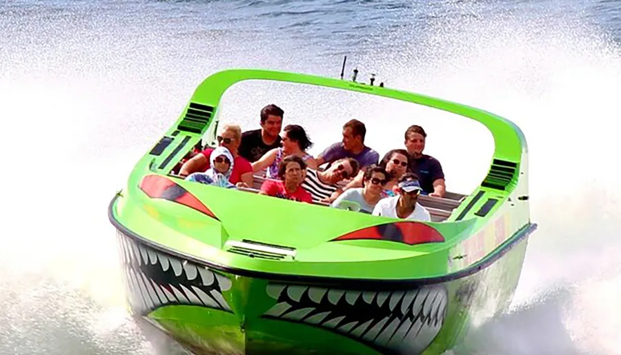 A group of people are experiencing a high-speed thrill ride on a boat designed to look like a menacing green creature with sharp teeth, spraying water behind as it races forward.