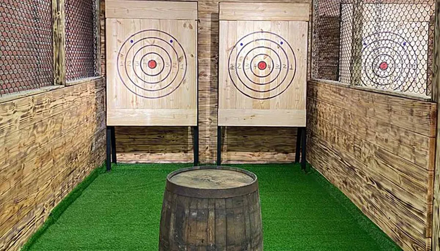 This image shows a setup of three axe-throwing targets in a rustic-themed area with artificial grass flooring and protective mesh on the sides.