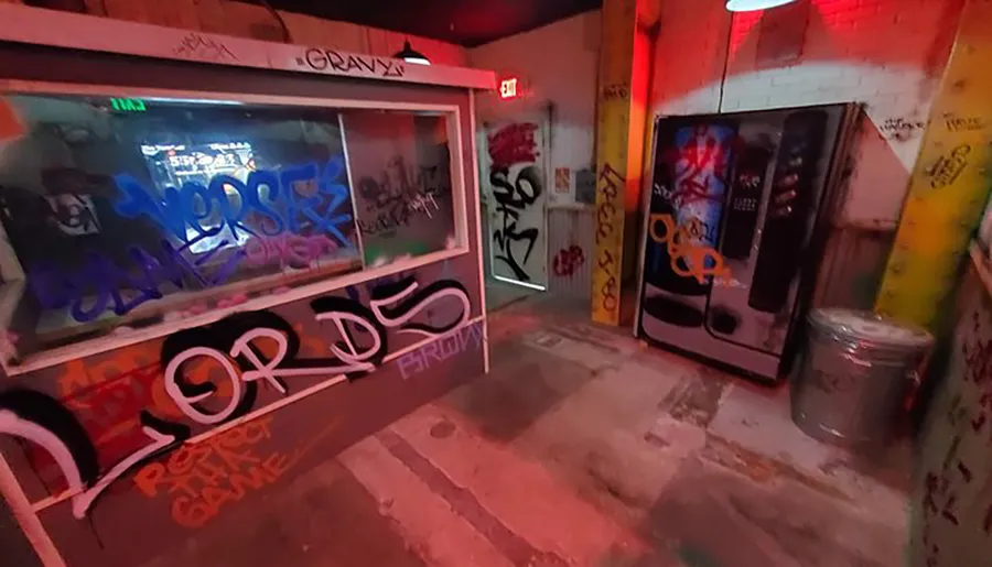 The photo shows a gritty urban scene with a vending machine and window covered in graffiti inside what appears to be a dimly lit alleyway or passageway with brick walls.
