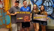 Four people are happily posing with signs indicating that they successfully completed an escape room challenge.