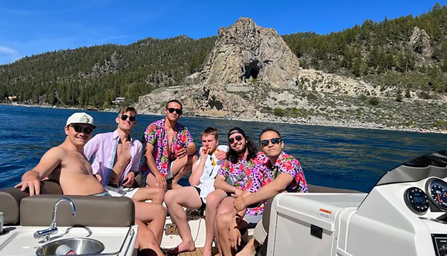 A group of friends wearing vibrant shirts is enjoying their time on a boat with a scenic rocky coastline in the background.