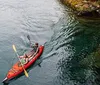 A person in a white sun hat is kayaking on a shimmering body of water surrounded by a forested area