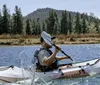 A person in a white sun hat is kayaking on a shimmering body of water surrounded by a forested area