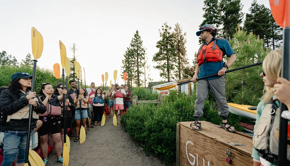 A group of people with paddles attentively listens to an instructor before a kayaking excursion