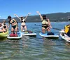 A group of people are enjoying paddleboarding and kayaking on a sunny day on a clear body of water with mountains in the background