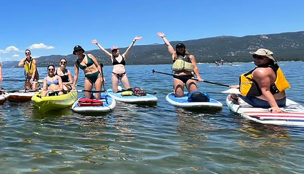 A group of people are enjoying paddleboarding and kayaking on a sunny day on a clear body of water with mountains in the background