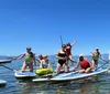 A group of people are enjoying paddleboarding and kayaking on a sunny day on a clear body of water with mountains in the background