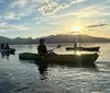 Three people are kayaking on a serene lake with mountains in the background as the sun sets creating a tranquil scene