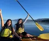 Two individuals are kayaking in a tandem yellow kayak on calm waters with mountains in the distance