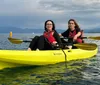 Two individuals are kayaking in a tandem yellow kayak on calm waters with mountains in the distance