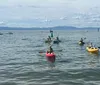 Two people are enjoying water sports on a calm lake with mountains in the background one kayaking and the other paddleboarding