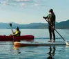 Two people are enjoying water sports on a calm lake with mountains in the background one kayaking and the other paddleboarding