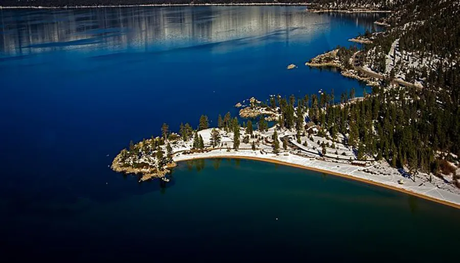 The image depicts a serene snow-dusted landscape featuring pine trees on a peninsula surrounded by the deep blue waters of a tranquil lake.